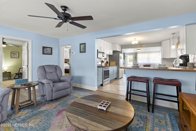 living area with baseboards, wood finished floors, and ceiling fan