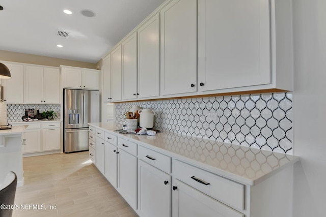 kitchen with light countertops, stainless steel fridge with ice dispenser, tasteful backsplash, visible vents, and white cabinets