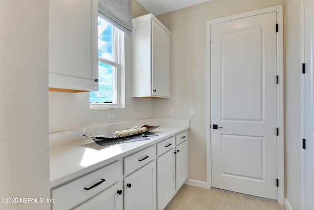 kitchen featuring white cabinets, light countertops, baseboards, and light wood-style flooring