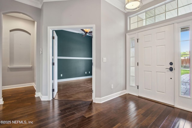 foyer entrance featuring crown molding, dark wood-style flooring, baseboards, arched walkways, and ceiling fan