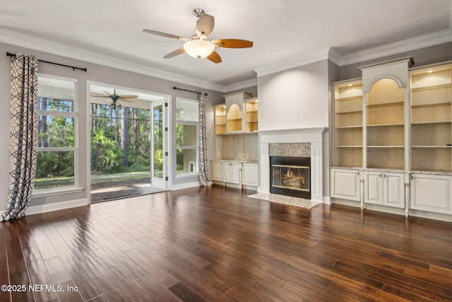 unfurnished living room featuring a high end fireplace, baseboards, ceiling fan, ornamental molding, and dark wood-type flooring