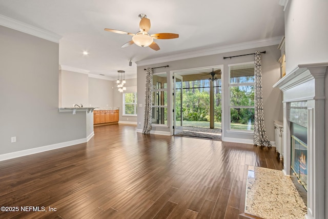 unfurnished living room featuring a fireplace with flush hearth, baseboards, ceiling fan with notable chandelier, ornamental molding, and dark wood-style flooring