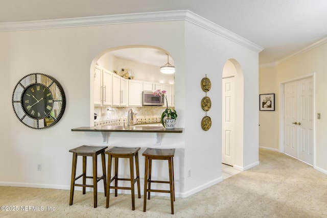 1825 Vista Cove Rd, Saint Augustine, FL 32084 - kitchen with stainless steel microwave, arched walkways, dark countertops, ornamental molding, and a kitchen breakfast bar