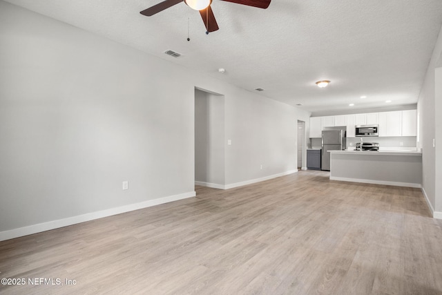 unfurnished living room with a textured ceiling, baseboards, visible vents, light wood-style floors, and ceiling fan