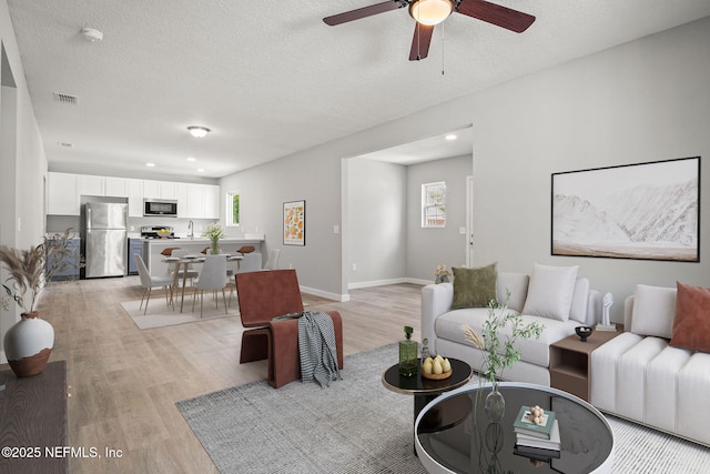 living room featuring visible vents, a healthy amount of sunlight, light wood-style floors, and a ceiling fan