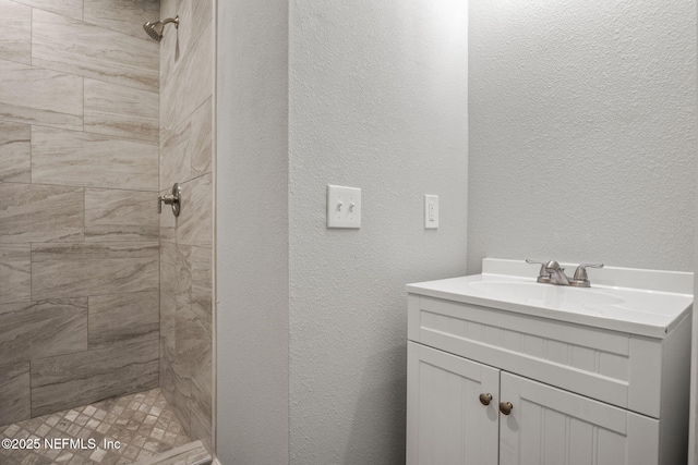 full bathroom with a tile shower, a textured wall, and vanity