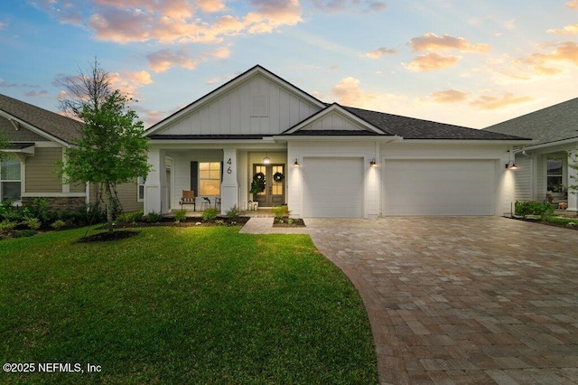 view of front of house with board and batten siding, decorative driveway, covered porch, a front lawn, and a garage
