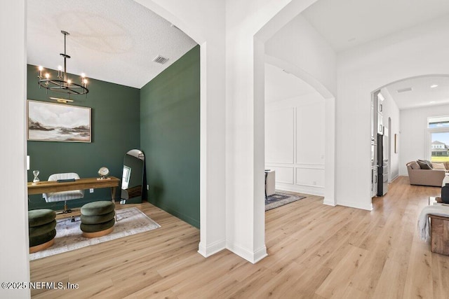 interior space featuring light wood finished floors, an inviting chandelier, visible vents, baseboards, and arched walkways