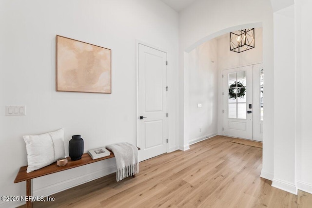 entrance foyer with arched walkways, an inviting chandelier, light wood-style flooring, and baseboards