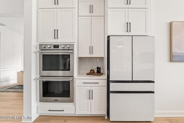 kitchen with double oven, light wood finished floors, and freestanding refrigerator