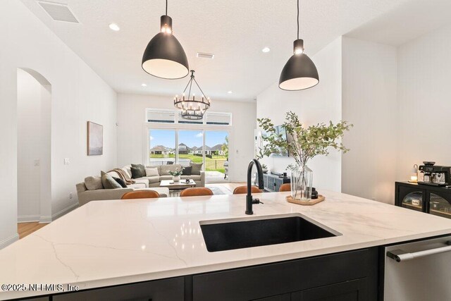kitchen featuring light stone counters, a sink, dark cabinets, open floor plan, and dishwasher