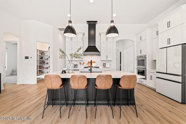 kitchen featuring arched walkways, light countertops, double oven, white fridge, and wall chimney exhaust hood