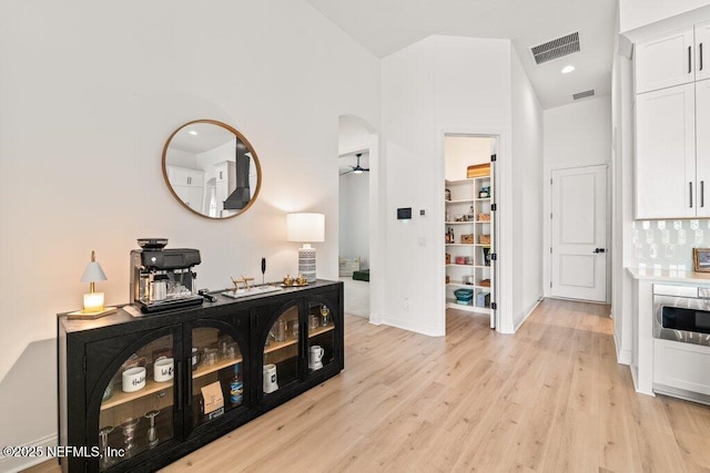 hall featuring visible vents, light wood-type flooring, arched walkways, and baseboards