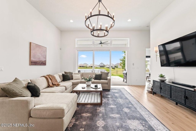 living area with recessed lighting, wood finished floors, an inviting chandelier, and a towering ceiling