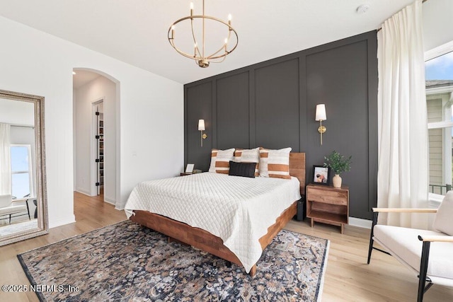 bedroom with baseboards, light wood-type flooring, arched walkways, and an inviting chandelier