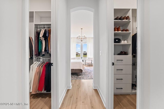 spacious closet with light wood finished floors and an inviting chandelier