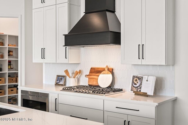 kitchen with custom exhaust hood, decorative backsplash, stainless steel gas cooktop, and white cabinets