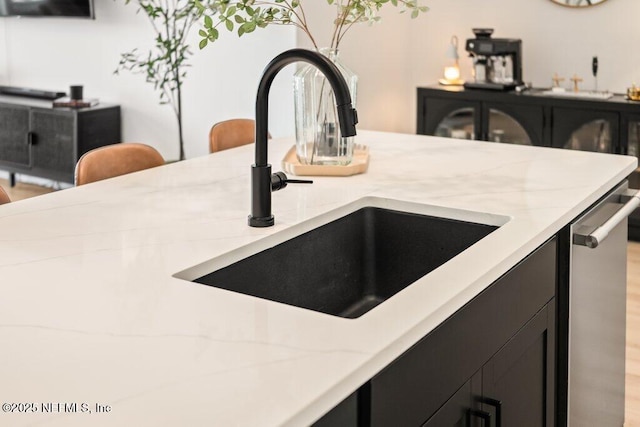 room details featuring light stone counters, dark cabinets, stainless steel dishwasher, and a sink