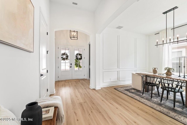 foyer featuring arched walkways, a decorative wall, light wood finished floors, visible vents, and a notable chandelier