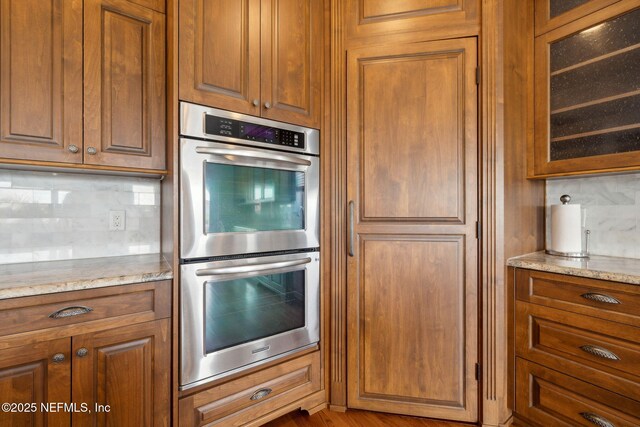 132 Beachside Dr, Ponte Vedra Beach, FL 32082 - kitchen with decorative backsplash, stainless steel double oven, brown cabinets, light stone countertops, and glass insert cabinets