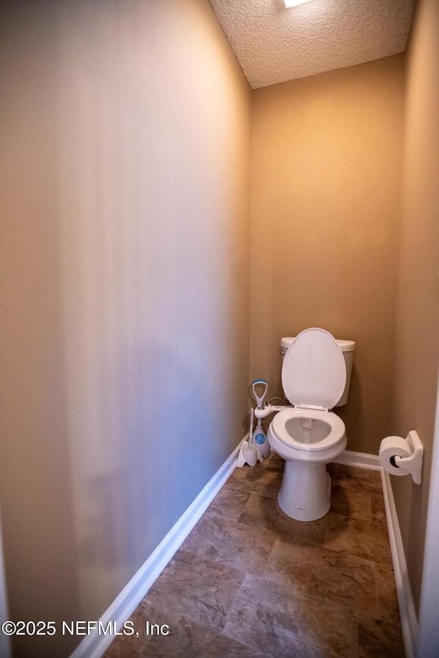 bathroom with toilet, a textured ceiling, and baseboards
