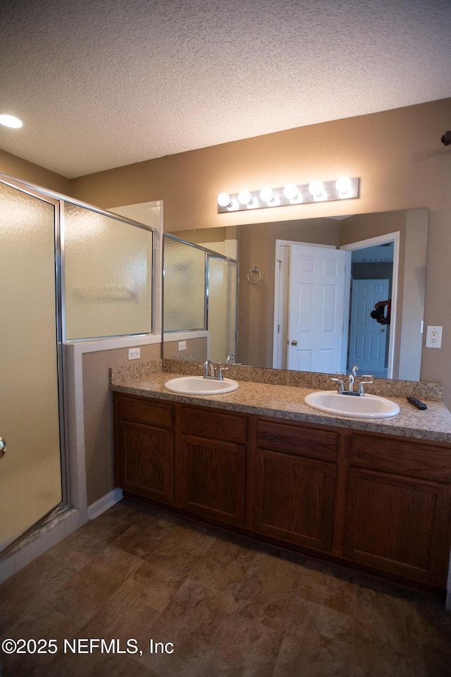 full bathroom featuring a shower stall, double vanity, a textured ceiling, and a sink