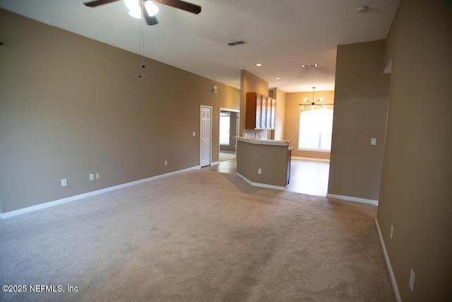 unfurnished living room featuring ceiling fan with notable chandelier, light colored carpet, baseboards, and visible vents