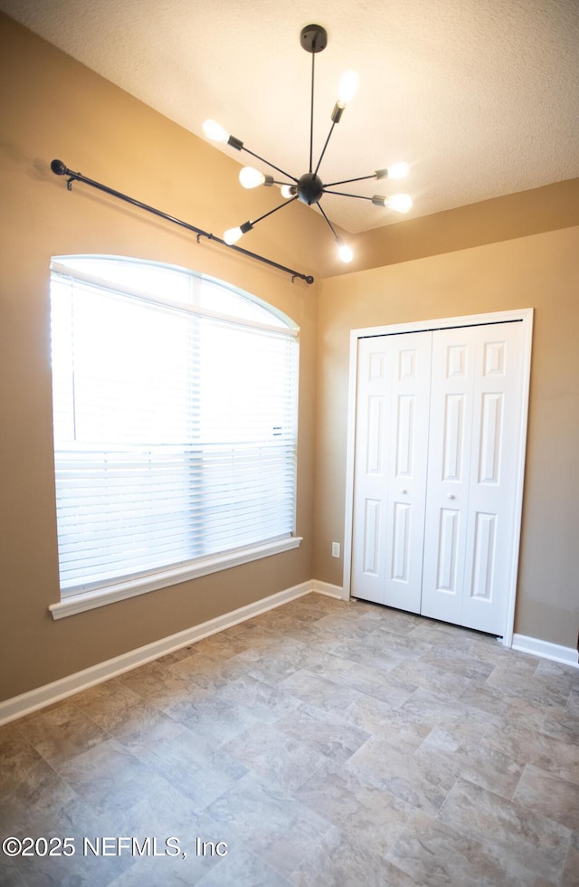 unfurnished bedroom featuring a chandelier, a closet, and baseboards