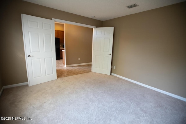 unfurnished bedroom featuring light carpet, visible vents, baseboards, and freestanding refrigerator
