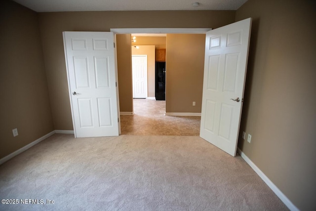 unfurnished bedroom featuring black refrigerator with ice dispenser, light colored carpet, and baseboards
