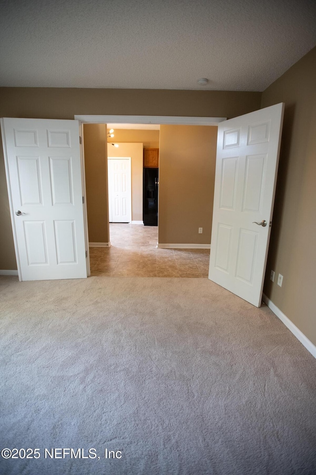empty room featuring baseboards, light tile patterned floors, light colored carpet, and a textured ceiling