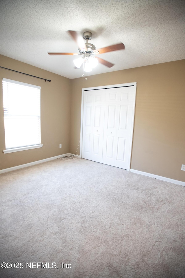 unfurnished bedroom featuring a closet, baseboards, a ceiling fan, carpet, and a textured ceiling
