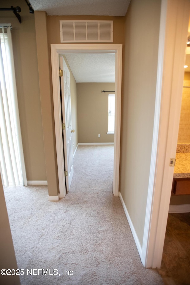 hallway featuring visible vents, baseboards, and carpet floors