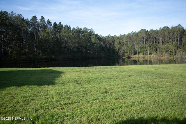view of yard with a wooded view and a water view