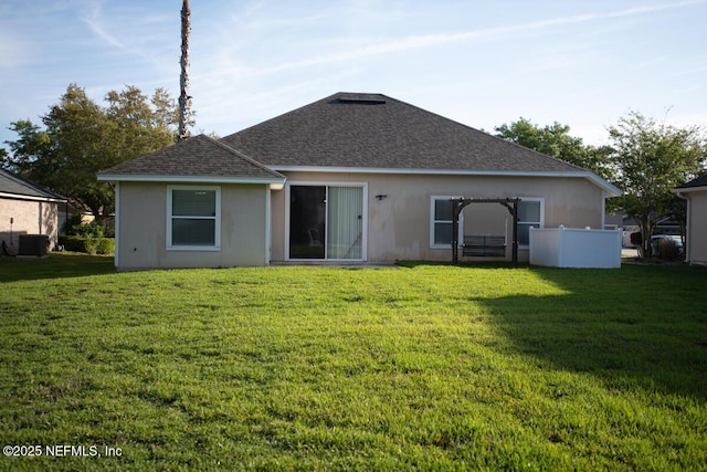 back of property with central AC, a shingled roof, a yard, and stucco siding
