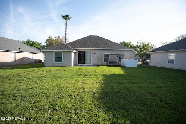 back of property featuring a shingled roof, stucco siding, and a lawn