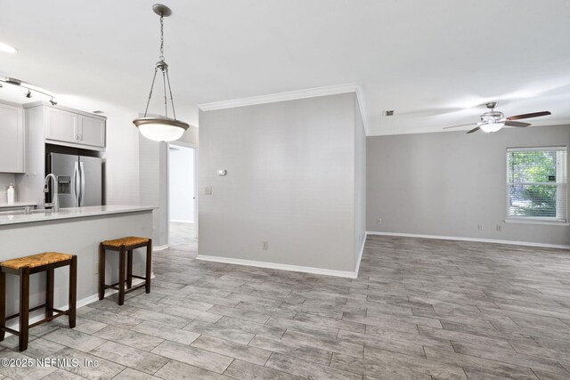 kitchen featuring pendant lighting, a kitchen bar, stainless steel fridge, light countertops, and a ceiling fan