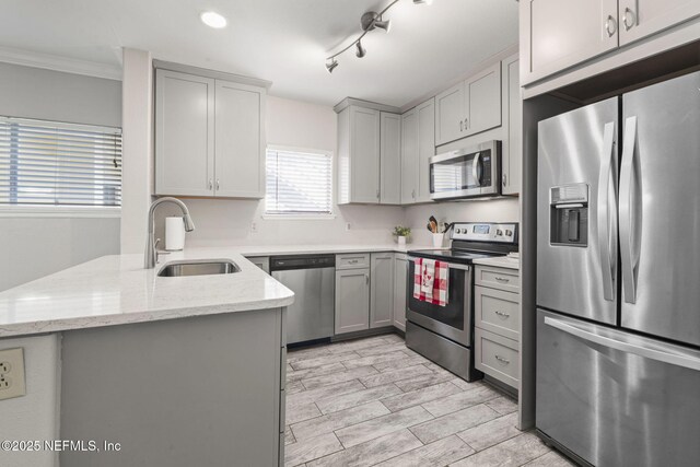 kitchen featuring appliances with stainless steel finishes, a sink, gray cabinetry, light stone counters, and a peninsula