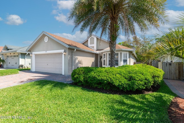 view of front of property with stucco siding, decorative driveway, a front yard, a garage, and fence