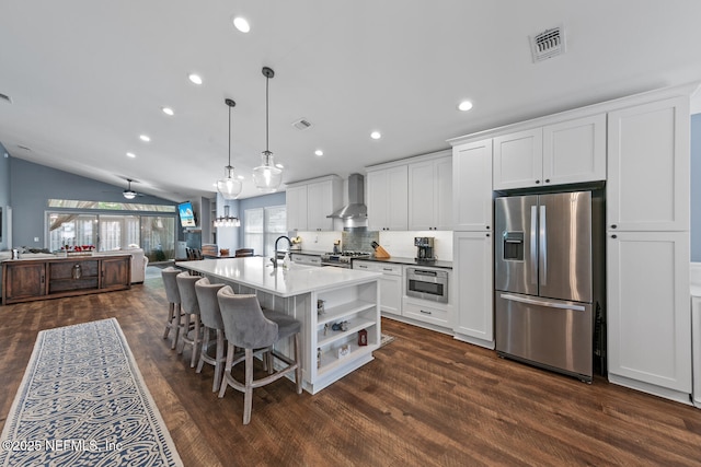 kitchen with visible vents, white cabinets, wall chimney exhaust hood, a sink, and appliances with stainless steel finishes