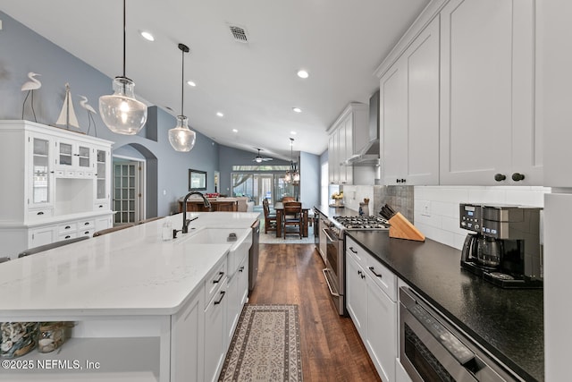 kitchen featuring dark wood-style flooring, stainless steel gas range oven, visible vents, wall chimney exhaust hood, and decorative backsplash
