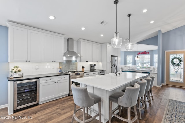 kitchen with tasteful backsplash, wall chimney range hood, appliances with stainless steel finishes, a kitchen bar, and wine cooler