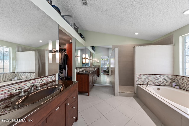 full bath with a sink, a walk in shower, a textured ceiling, and a healthy amount of sunlight