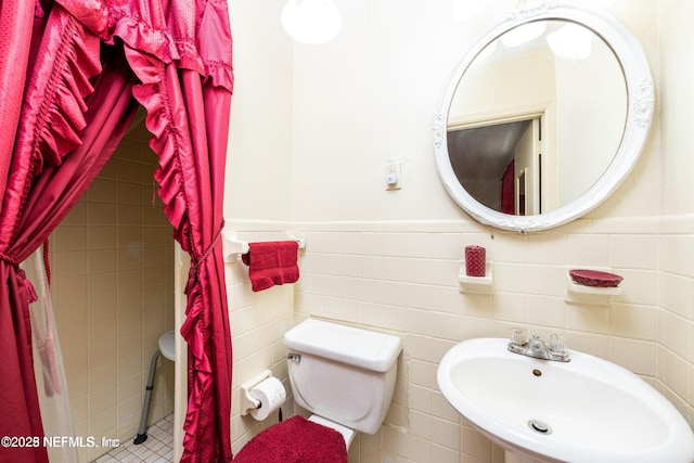 bathroom featuring tile walls, wainscoting, toilet, and a sink
