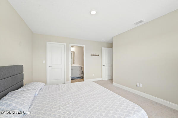 73 Lily Landing Dr, Saint Augustine, FL 32092 - bedroom featuring ensuite bathroom, baseboards, light colored carpet, and visible vents