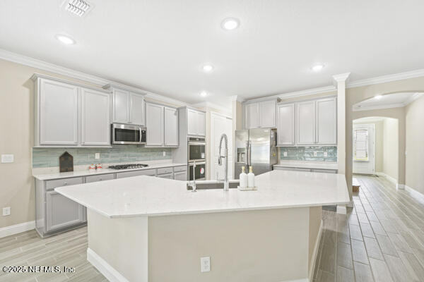 73 Lily Landing Dr, Saint Augustine, FL 32092 - kitchen with crown molding, a large island with sink, light countertops, stainless steel appliances, and arched walkways