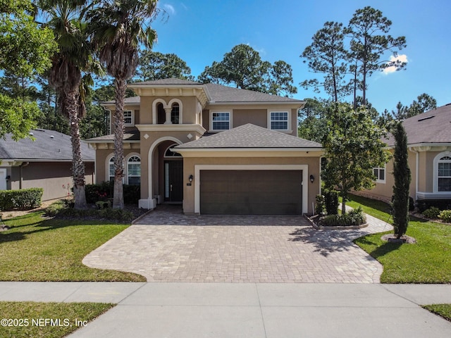 mediterranean / spanish home featuring an attached garage, decorative driveway, a front lawn, and stucco siding
