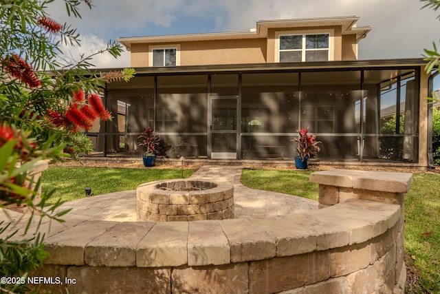 back of house featuring a sunroom, a fire pit, stucco siding, and a patio area