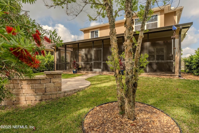 rear view of house featuring a yard, stucco siding, and a sunroom