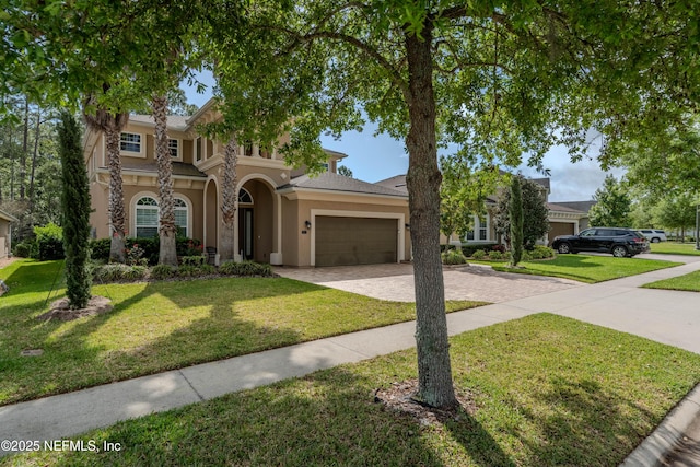 view of front of property featuring a garage, decorative driveway, stucco siding, and a front yard